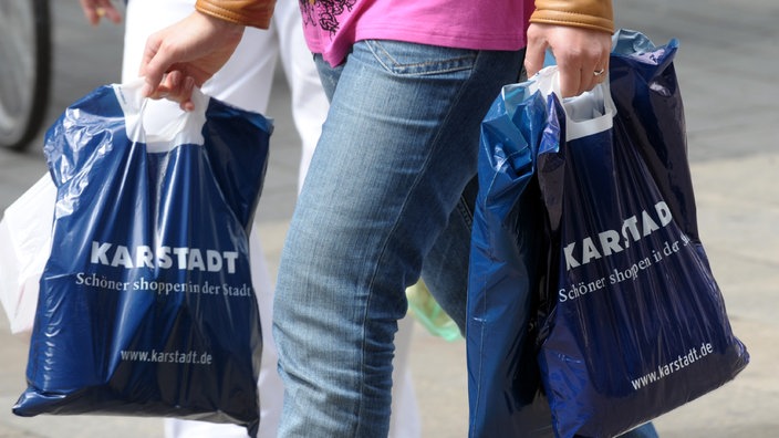 Hände eines Mannes tragen zwei Plastiktüten mit Werbeaufdruck von Karstadt