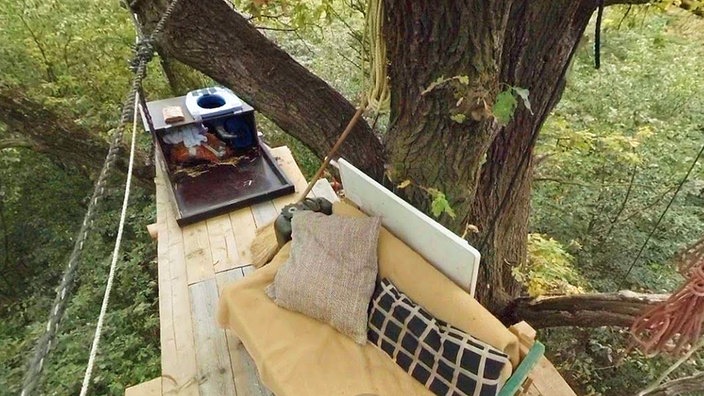 Blick auf einen Plattform eines Baumhauses im Hambacher Forst, im Hintergrund ist eine Toilette zu sehen.