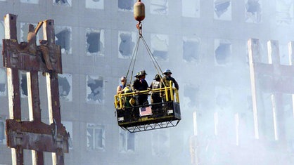 Feuerwehrmänner schweben in einem Korb an einem Kran über das Trümmerfeld 