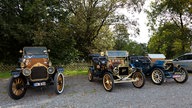 Drei Oldtimer stehen nebeneinander auf einem Parkplatz