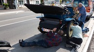 Mehrere Männer knien neben einem defekten Oldtimer