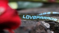 Eine rote Rose und ein Stoffband mit der Aufschrift "Loveparade"