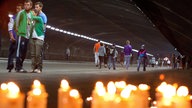 Jugendliche gehen durch einen Tunnel, vor dem viele Kerzen brennen