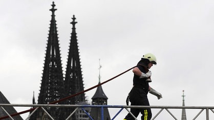 Feuerwehrmann zieht Schlauch vor der Dom-Silhouette