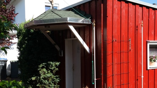 Kleines Holzhaus mit überdachtem Eingangsbereich und Glöckchen darüber 