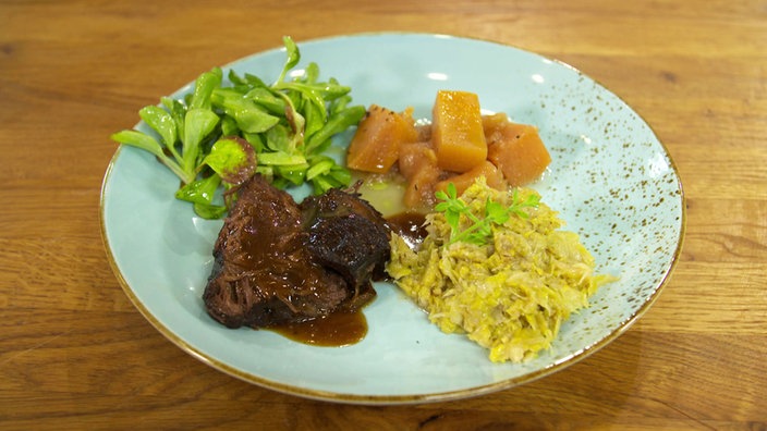 Das Bild zeigt das fertige Gericht Ochsenbäckchen mit Rosenkohl-Püree, Steckrüben-Apfel-Gemüse und Feldsalat mit Kartoffelvinaigrette.