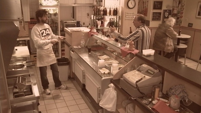 Aufnahme des Imbiss von innen. Dittsche und Ingo stehen an der Theke und unterhalten sich im Hintergrund sitzt Kröti.