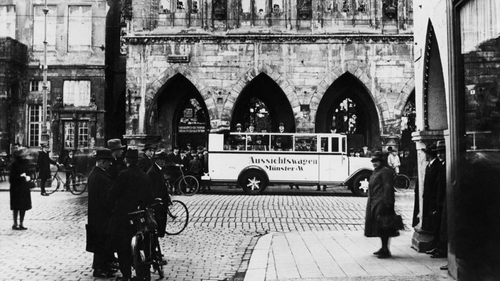 Der Prinzipalmarkt in Münster abends, mit golden beleuchteten Häusern und der Lambertikirche im Hintergrund