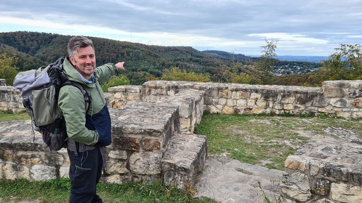 Moderator Hendrik Schulte steht auf einem Hügel und zeigt in Richtung des Teutoburger Waldes