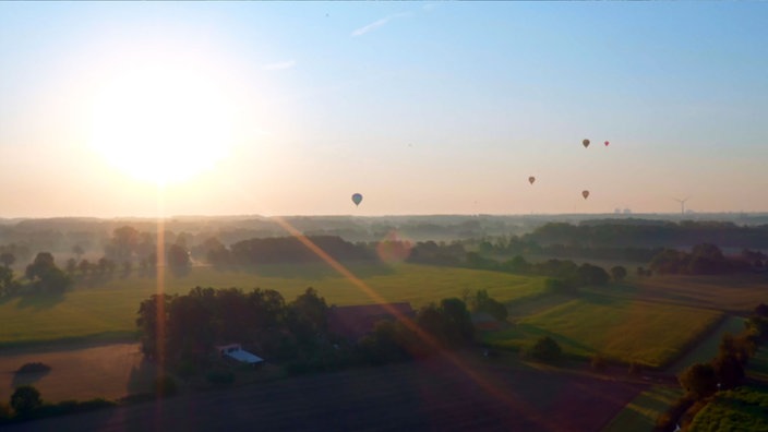 Totale Lauftaufnahme: Heißluftballons über einer Wisenlandschaft.