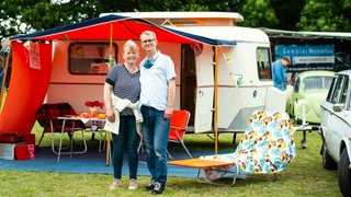 Ein Pärchen steht vor ihrem Wohnwagen und lächelt in die Kamera