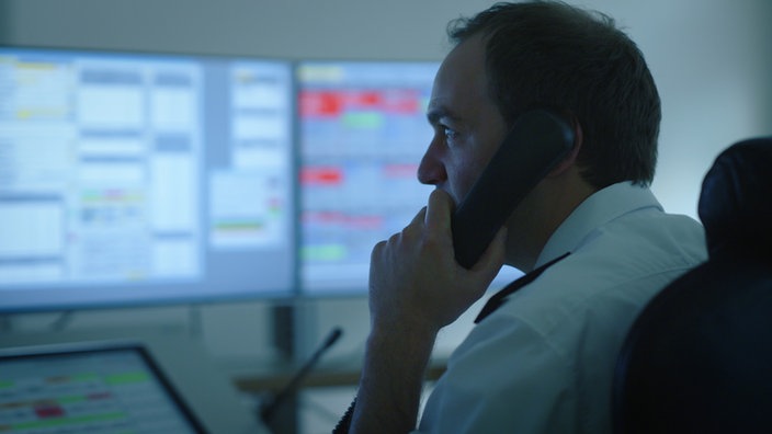 Ein Mann sitzt telefonierend in der Leitzentrale der Düsseldorfer Feuerwehr, im Hintergrund Monitore