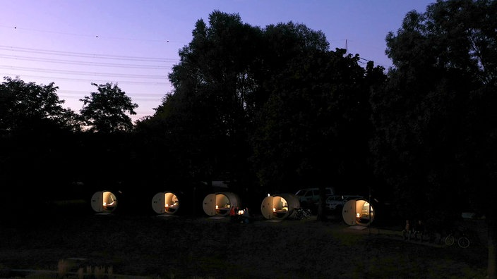 Abendstimmung, 5 große beleuchtete Betonröhren unter Bäumen