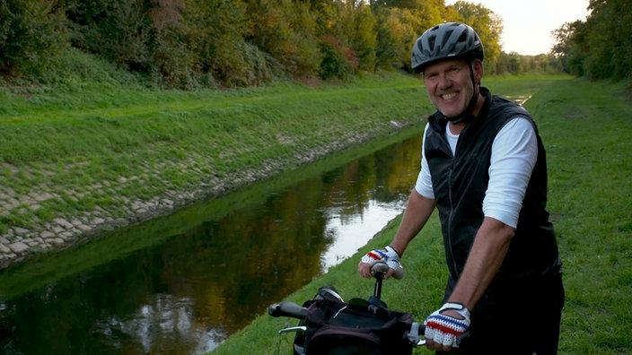 Ein Mann mit Fahhrad steht an einem Fluss