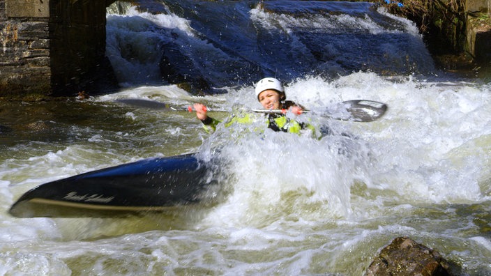 Eine Sportlerin im Kajak befährt eine Stromschnelle