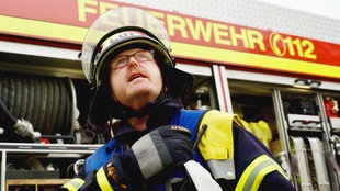 Ein Feuerwehr-Mann in voller Ausrüstung steht vor einem Feuerwehrwagen