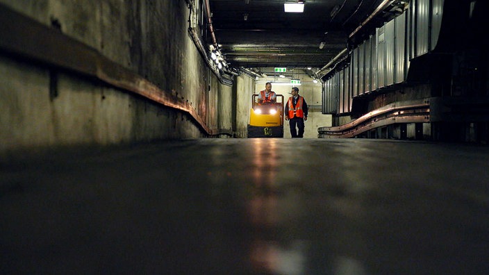 Zwei Arbeiter fahren mit einem Elektrokarren durch einen Versorgungstunnel