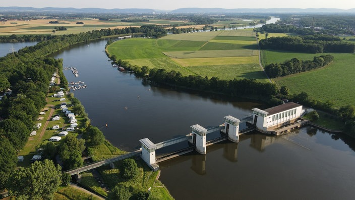 Blick aus der Luft über eine grüne Landschaft mit einem Fluss und dem Stauwehr in Petershagen.