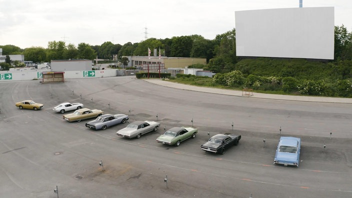 Luftaufnahme vom Autokino mit vielen US-Oldtimern in der ersten Reihe vor der Leinwand.