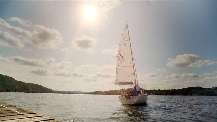 Ein Segelbott mitten auf dem Baldeneysee mit zwei Personen an Bord.