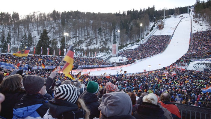 Zuschauermenge jubelt, im Hintergrund die Auslaufzone der Sprungschanze