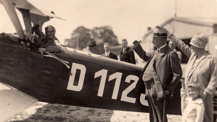 Thea Rasche winkend im offenen Flugzeug beim Start