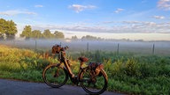 Ein Fahrrad vor Feldern im morgendlichen Dunst.