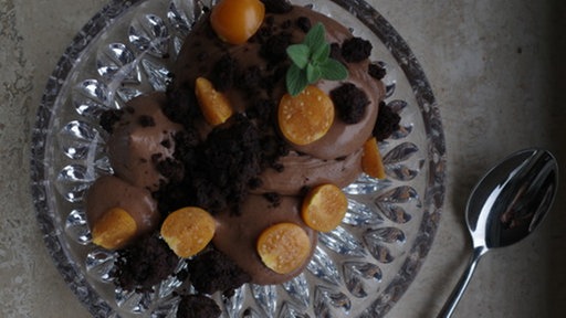 Nougatmousse in einem Glas mit Schoko-Crumble, daneben ein Löffel