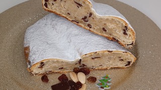 Aufgeschnittener Quarkstollen mit Marzipan auf einem goldenen Teller mit weihnachtlicher Deko.