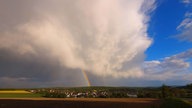 Eine Wetterfront zieht über ein Dorf hinweg und bildet einen Regenbogen.