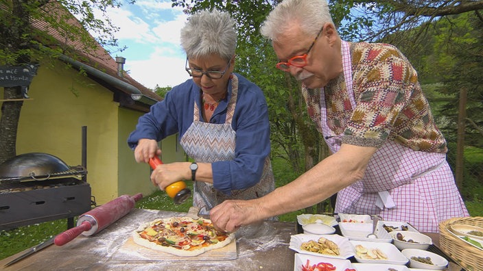 Martina und Moritz belegen eine Pizza am Grill