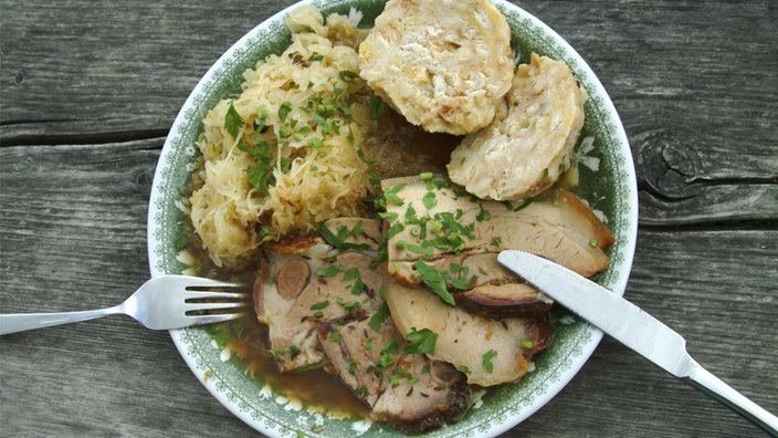 Schweinebraten, Sauerkraut und Knödel auf einem Teller angerichtet