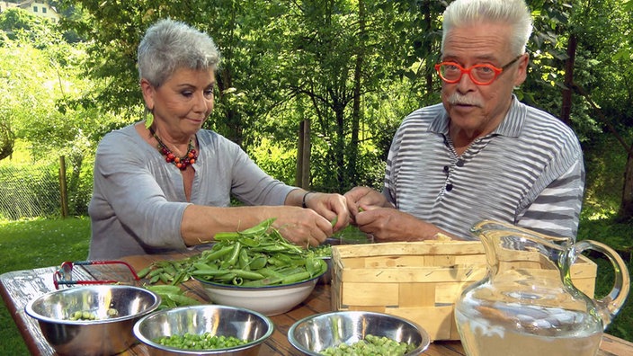 Martina Meuth und Bernd Neuner-Duttenhofer sitzen an einem Gartentisch und pulen Erbsen aus