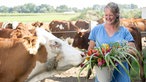 Anna Pröbstle mit Kühen und einem Eimer voller Wildblumen. 