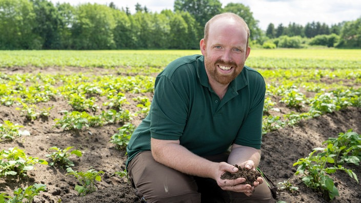 Rainer Overkämping mit einer Handvoll Erde auf dem Feld. 