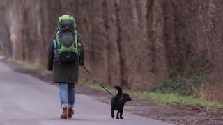 Britta Düsterhus mit Rucksack und Hund auf einer Straße