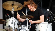 Der Johnossi-Drummer schlägt auf die Becken seines Schlagzeuges. Seine Haare fliegen wild nach vorne