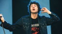 Der Sänger der Band "The Kooks" hält den Mikrofonständer mit der linken Hand und einen Finger der anderern Hand an das Ohr.