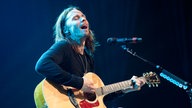 Myles Kennedy sitzt auf einem Hocker und singt mit geschlossenen Augen, während er sich selbst mit der Gitarre begleitet