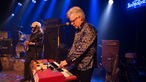 Organist von Big Sugar steht an seiner roten elektrischen Orgel und spielt und blickt konzentriert auf sein Instrument, im Hintergrund sind Bassist und Schlagzeuger zu sehen