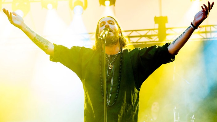 Der Sänger von Orphaned Land am Mikro vor einem strahlend gelben Licht