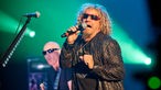 Der Sänger von Chickenfoot hält sich das Mikrofon an den Mund und winkelt den linken Arm an im Hintergrund ist der Gitarrist der Band zu sehen