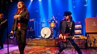 Sänger von "Rival Sons" singt mit Tamburin in der Hand, neben ihm der Gitarrist und im Hintergrund der Schlagzeuger im blauen Licht.