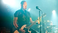 Der Frontmann des Trios ist auf das Gitarre spielen konzentriert.