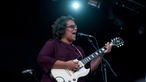 Sängerin der Alabama Shakes im violetten Kleid singt in ein Mikrofon und spielt Gitarre