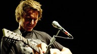 Ben Howard spielt auf der Gitarre und steht vor einem Mikrofon