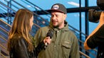 Frau mit langen braunen Haaren interviewt Mann mit LA Clippers Kappe 