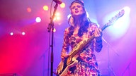 Kate Nash hat einen Bass vor sich hängen und sieht weiter über der Kamera hinweg.