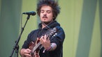 Clemens von Milky Chance, dessen Haarfrisur an Mecki den Igel erinnert, spielt konzentriert Gitarre. Den Blick hat er auf sein Instrument gesenkt.