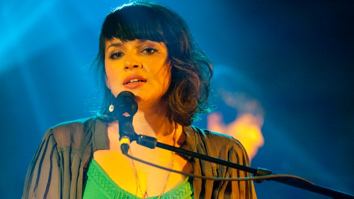 Norah Jones sitzt vor dem Mikrofon und singt einen Song